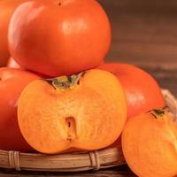 Fresh beautiful sliced sweet persimmon kaki on dark wooden table with red brick wall background, Chinese lunar new year fruit design concept, close up. photo