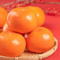 Fresh beautiful sliced sweet persimmon kaki isolated on red table background and bamboo sieve, Chinese lunar new year design concept, close up. photo