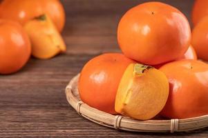 Fresh, beautiful orange color persimmon kaki on bamboo sieve over dark wooden table. Seasonal, traditional fruit of Chinese lunar new year, close up. photo