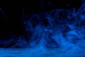 Conceptual image of blue smoke isolated on dark black background and wooden table. photo