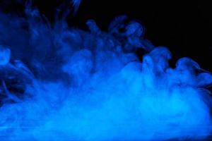 Conceptual image of blue smoke isolated on dark black background and wooden table. photo