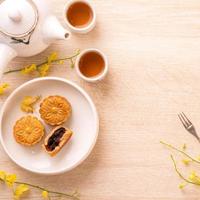 sabroso pastel de luna para el festival de mediados de otoño en una mesa de madera brillante, concepto de té festivo decorado con flores amarillas, vista superior, puesta plana. foto