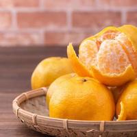 Peeled tangerines in a bamboo sieve basket on dark wooden table with red brick wall background, Chinese lunar new year fruit design concept, close up. photo