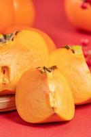 Fresh beautiful sliced sweet persimmon kaki isolated on red table background and bamboo sieve, Chinese lunar new year design concept, close up. photo