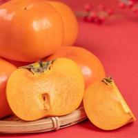 Fresh beautiful sliced sweet persimmon kaki isolated on red table background and bamboo sieve, Chinese lunar new year design concept, close up. photo