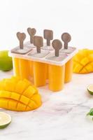 Fresh mango fruit popsicle ice in the plastic shaping box on bright marble table. Summer mood concept product design, close up. photo
