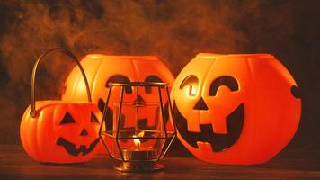 Halloween concept - Orange plastic pumpkin lantern with laugh face on a dark wooden table with smoke around the background, trick or treat, close up. photo