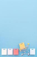 elemento de diseño abstracto, venta anual, concepto de temporada de compras, mini carro amarillo con bolsa de papel de colores sobre fondo azul pastel, vista superior, puesta plana foto