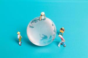 Miniature people cleaning crystal globe on blue background photo