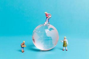 Miniature people cleaning crystal globe on blue background photo