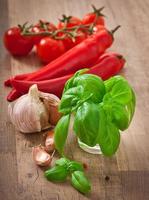 Red chili peppers, tomatoes, garlic and basil on a wooden background