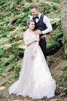 Attractive couple newlyweds, happy and joyful moment. Man and woman in festive clothes sit on the stones near the wedding decoration in boho style. Ceremony outdoors. photo