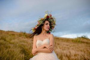 the bride in a beautiful blue dress with a deep neckline at the back with a wreath on her head of white flowers stands on a background of mountains and lakes