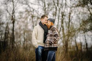 feliz pareja enamorada en otoño. un hombre con bigote de cabello rizado y una mujer de cabello rojizo con chaquetas de cuero y jeans se abrazan tiernamente. chica hace palmas de corazón foto