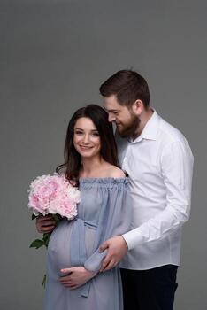 A pregnant woman and her husband are hugging on a gray background in the studio. photo