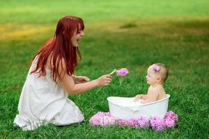 Mom helps her little one-year-old daughter bathe in the bathroom. Filmed in a park outdoors in nature. photo