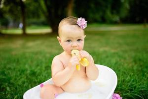 Little girl bathes in a milk bath in the park. The girl is having fun in the summer.