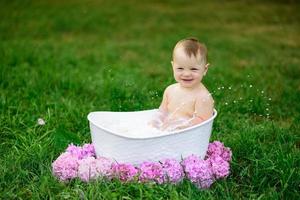 Little girl bathes in a milk bath in the park. The girl is having fun in the summer. photo