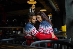 joven pareja amorosa vestida con suéter azul sentada con tazas de café tejidas en el café en invierno