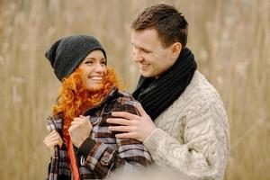 happy couple in love in autumn. curly-haired mustachioed man and ruddy-haired woman in leather jackets and jeans tenderly embrace. girl makes palms of heart photo