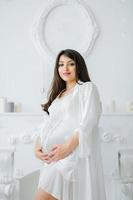 Portrait of young pregnant attractive woman, standing by the window, dressed in casual clothing, day before due date photo