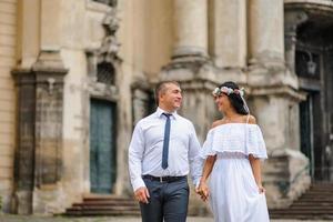 Wedding photo session on the background of the old building. The groom watches his bride posing. Rustic or boho wedding photography.