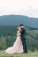 La novia y el novio jóvenes y elegantes se paran en un bote en el fondo del cielo nublado, el mar y las montañas de montenegro. foto