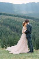 La novia y el novio jóvenes y elegantes se paran en un bote en el fondo del cielo nublado, el mar y las montañas de montenegro. foto