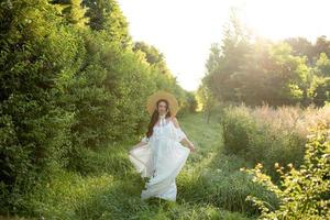 Pregnant woman in a hat posing in a dress on a background of green trees. photo