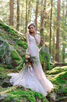 Happy bride in a pink wedding dress. The girl holds a wedding bouquet in her hands. Boho style wedding ceremony in the forest. photo
