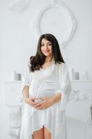 Portrait of young pregnant attractive woman, standing by the window, dressed in casual clothing, day before due date photo