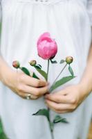 Female hand holding beautiful bouquet with fragrant peonies on light background photo