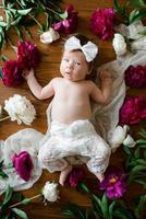 una niña de dos meses yace sobre una mesa con peonías. foto