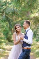 una atractiva pareja de recién casados, un momento feliz y alegre. un hombre y una mujer se afeitan y se besan con ropa de fiesta. ceremonia de boda de estilo bohemio en el bosque al aire libre. foto