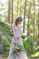 Happy bride in a pink wedding dress. The girl holds a wedding bouquet in her hands. Boho style wedding ceremony in the forest. photo