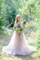 Happy bride in a pink wedding dress. The girl holds a wedding bouquet in her hands. Boho style wedding ceremony in the forest. photo