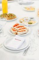 Round dinner tables covered with blue cloth stand in a white wedding pavilion photo