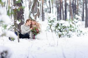 la novia y el novio están sentados en el tronco en el bosque de invierno. de cerca. ceremonia de boda de invierno. foto