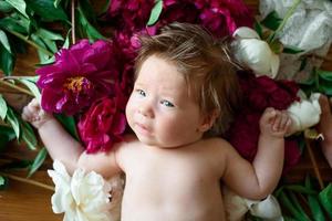 A little two-month-old girl lies on a table with peonies. photo