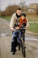 Couple in love is riding the bicycle in the park. Active people. Outdoors. Autumn couple wearing in autumn clothes. Funny couple are getting ready for autumn sale photo