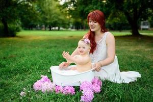 Mom helps her little one-year-old daughter bathe in the bathroom. Filmed in a park outdoors in nature. photo
