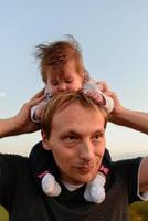 una pequeña hija linda se sienta en su cuello cerca de su padre. padre e hija están caminando en el campo foto