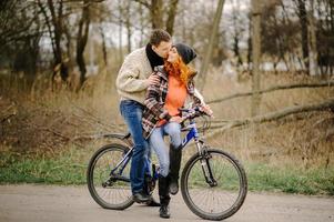Couple in love is riding the bicycle in the park. Active people. Outdoors. Autumn couple wearing in autumn clothes. Funny couple are getting ready for autumn sale photo