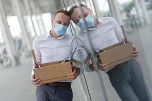 The fired office worker fell to his knees and covered his face due to stress. In front of him is a cardboard box with stationery. The man is unhappy due to a reduction in the robot. photo