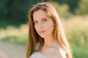 retrato de una joven hermosa en un vestido de verano. sesión de fotos de verano en el parque al atardecer. una niña se sienta debajo de un árbol a la sombra.