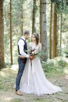 atractiva pareja de recién casados, momento feliz y alegre. el hombre y la mujer con ropa festiva se sientan en las piedras cerca de la decoración de la boda al estilo boho. ceremonia al aire libre. foto