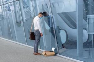 The fired office worker fell to his knees and covered his face due to stress. In front of him is a cardboard box with stationery. The man is unhappy due to a reduction in the robot. photo