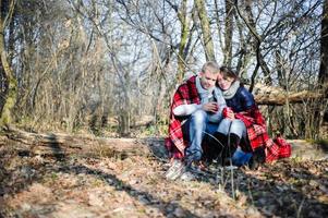 una pareja bastante joven relajándose cerca de la hoguera en el bosque al atardecer foto