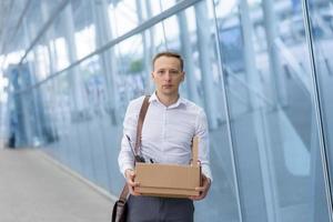 Dismissed office worker holds stationery in his hands in a cardboard box. The man is unhappy due to a reduction in the robot. photo