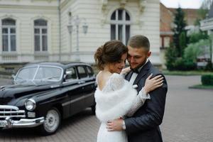 Happy luxury wedding couple kissing and embracing near retro with bouquet car in autumn photo